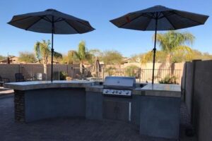 A grill and two umbrellas in the middle of an outdoor patio.