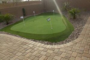 A backyard with a putting green and a brick patio.