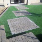 A walkway with brick pavers and artificial grass.