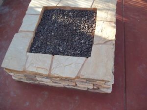 A square fire pit with black rocks in it.