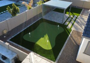 A backyard with a putting green and a pool.