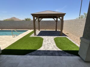 A gazebo with grass and pavers next to the pool.