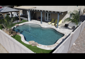 A pool with grass and chairs around it