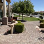 A brick patio with bushes and trees in the background.